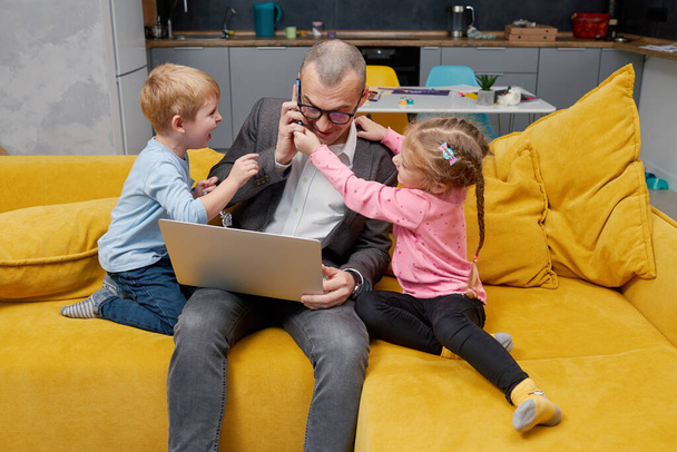 Father working from home with kids during quarantine lockdown and closed school. coronavirus outbreak. Young businessman freelancer works on laptop with children playing around. - Foto, imagen