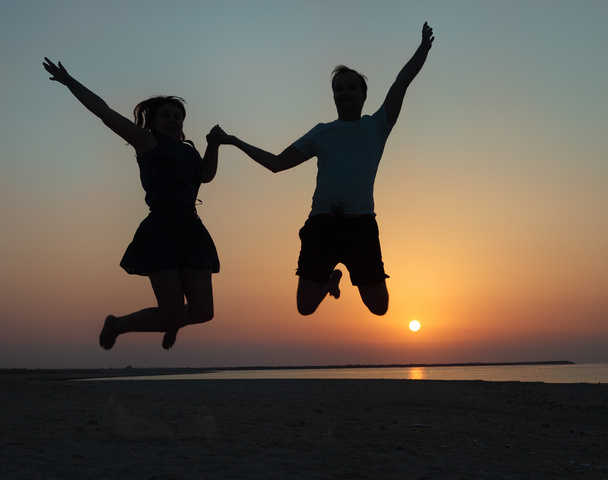 Silhouette of a couple - man and woman jumping on the beach  - Foto, afbeelding