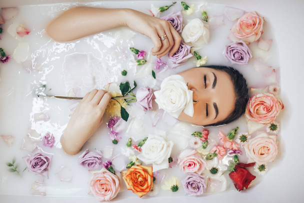 La femme prend un bain de bien-être rempli de lait. Les bourgeons de roses multicolores flottent à la surface. Traitements relaxants et anti-âge.. - Photo, image