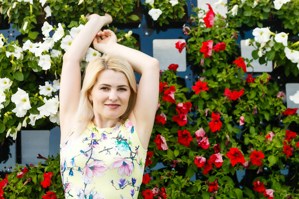 Beautiful young woman in nice dress posing on colorful wall of flowers. Fashion photo, nice hair, big smile - Photo, Image