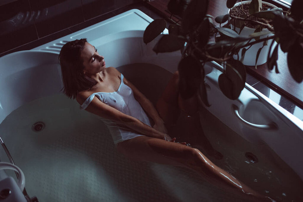 A young beautiful girl, in a white T-shirt and thin linen in a bathroom, in a jacuzzi, she is wearing a wet burner on her body, nude - Фото, зображення