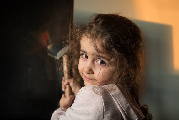 Χαριτωμένο κοριτσάκι στέκεται μπροστά από μια τηλεόραση με σπασμένη οθόνη κρατώντας ένα σφυρί. Οικογενειακή ασφάλεια. Παιδικό σπασμένο οδήγησε οθόνη τηλεόρασης με ένα σφυρί - Φωτογραφία, εικόνα