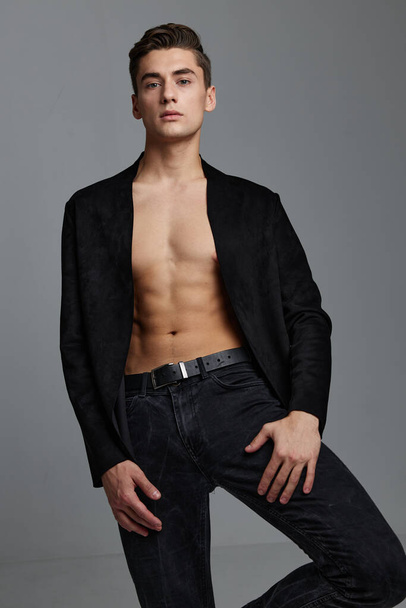 A sexy man in a buttoned jacket with a naked torso holds his hand near his leg - Photo, Image