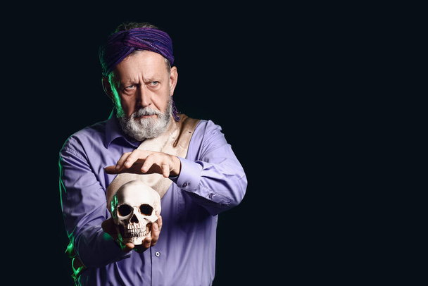 Male fortune teller with human skull on dark background - Photo, Image
