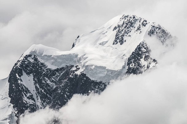 Atmospheric minimalist alpine landscape with massive hanging glacier on snowy mountain peak. Big balcony serac on glacial edge. Low clouds among snowbound mountains. Majestic scenery on high altitude. - Foto, Imagen