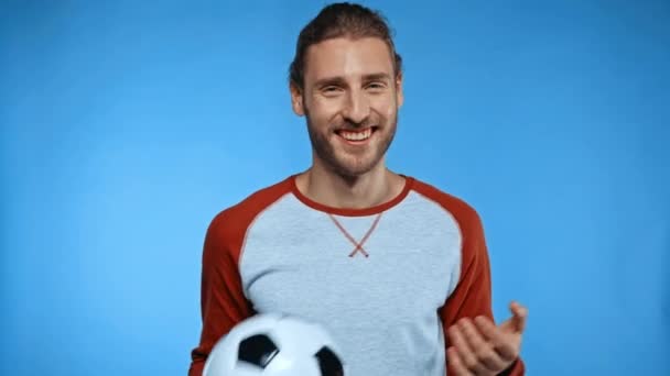 alegre hombre con pelota de fútbol mostrando ven conmigo gesto aislado en azul - Metraje, vídeo