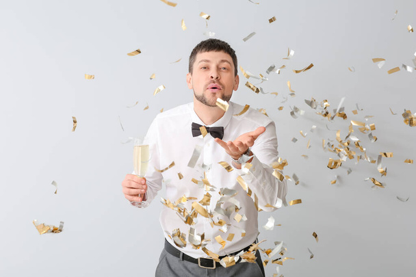Happy man with champagne and falling confetti on light background - Foto, Imagen