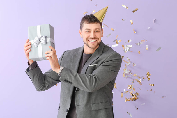 Happy man with gift and falling confetti on color background - Photo, Image
