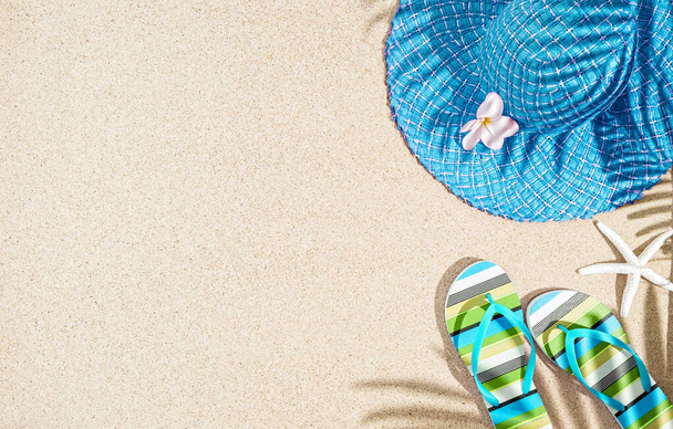 Große runde blaue Sommermütze und bunt gestreifte Sandalen auf Sand mit Palmenschatten, tp-Ansicht, Kopierraum  - Foto, Bild