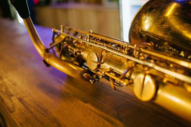 Close-up foto van een glanzende gouden saxofoon. Vintage saxofoon. Gouden sopraan saxofoon. Blaasinstrument. Prachtige gouden saxofoon op houten achtergrond - Foto, afbeelding