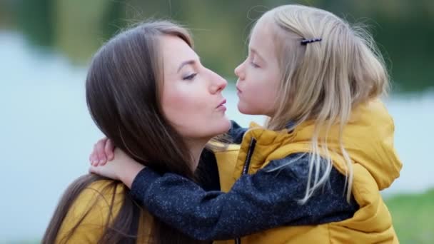 Hija besando a la madre en la naturaleza. Hermosa joven y su encantadora hijita se abrazan y sonríen. Hija abrazando madre en la naturaleza. - Imágenes, Vídeo