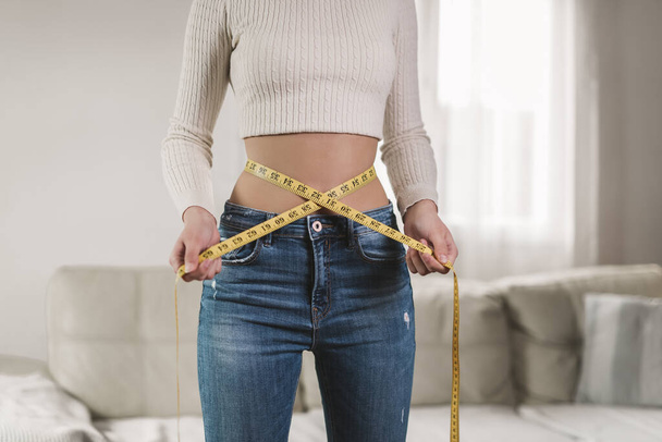 Concept of healthy eating. Young girl with perfect waist with a measuring tape in hands - Photo, Image
