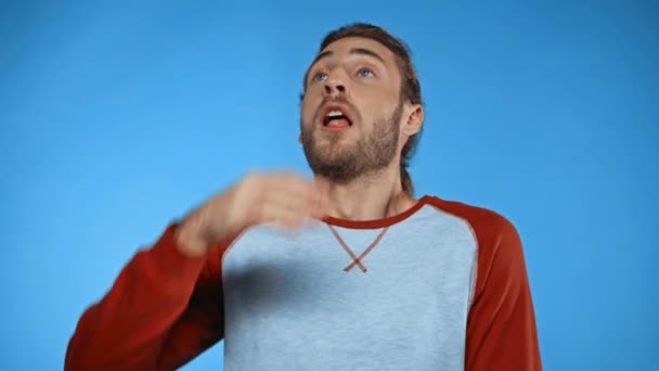 hombre enfermo estornudando y limpiando la mano y la nariz con jersey aislado en azul - Metraje, vídeo