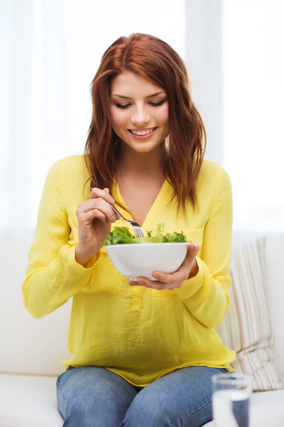 Smiling young woman with green salad at home - Foto, Bild