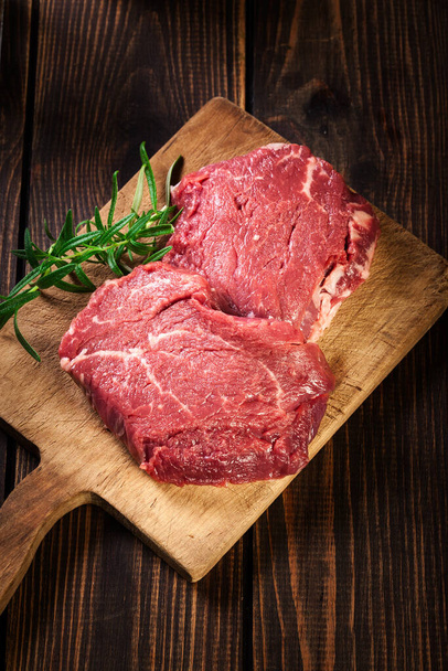 Fresh raw beef steak sirloin with rosemary on cutting board. Top view - Fotografie, Obrázek