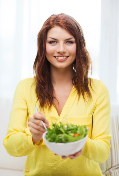 Smiling young woman with green salad at home - Foto, Imagem