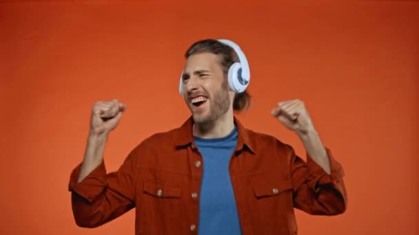 energizovaný muž zpívá a tančí ve sluchátkách izolovaných na oranžové - Záběry, video