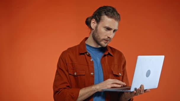 στοχαστικός ελεύθερος επαγγελματίας δακτυλογράφηση σε φορητό υπολογιστή απομονωμένο σε πορτοκαλί - Πλάνα, βίντεο