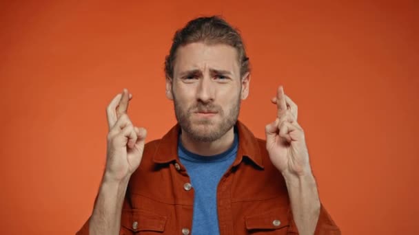 gespannen man met gekruiste vingers geïsoleerd op oranje - Video