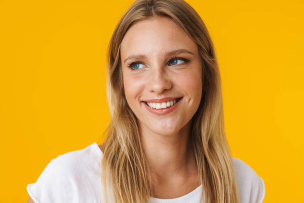 Cheerful beautiful girl smiling and looking aside isolated over yellow background - Photo, Image