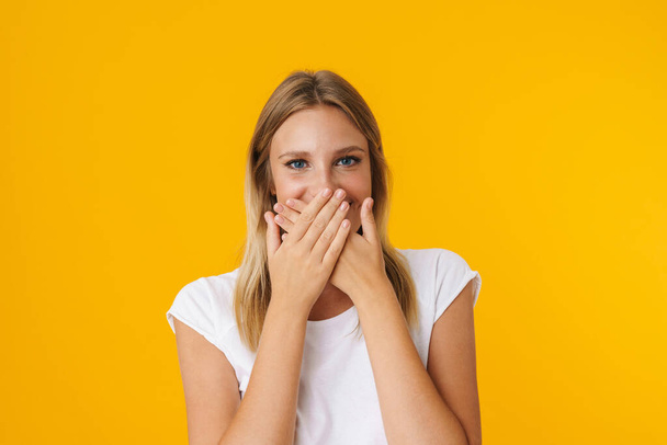Cheerful beautiful girl posing and covering her mouth isolated over yellow background - Foto, Bild