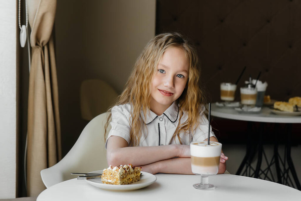 A cute little girl is sitting in a cafe and looking at a cake and cocoa close-up. Diet and proper nutrition - Foto, Bild