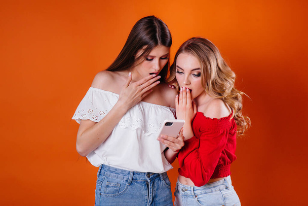 Dos chicas jóvenes y hermosas se toman una selfie y miran el teléfono en el estudio sobre un fondo púrpura. Chicas para la publicidad - Foto, imagen