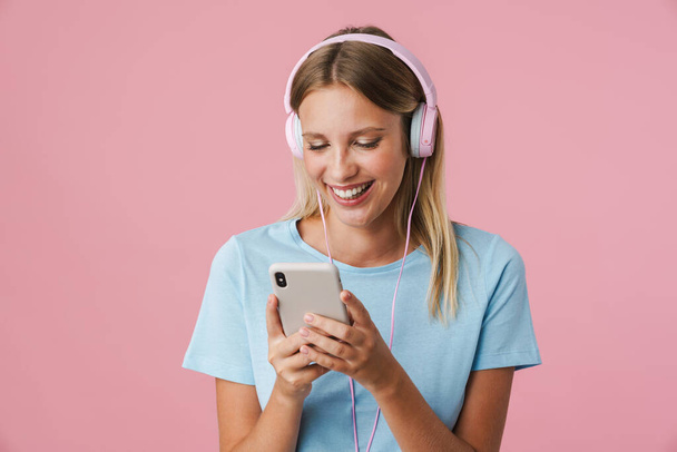 Portrait of a happy woman listening to music in headphones isolated on pink background - Foto, imagen