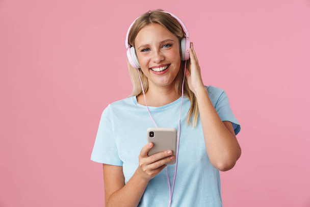 Portrait of a happy woman listening to music in headphones isolated on pink background - Photo, image