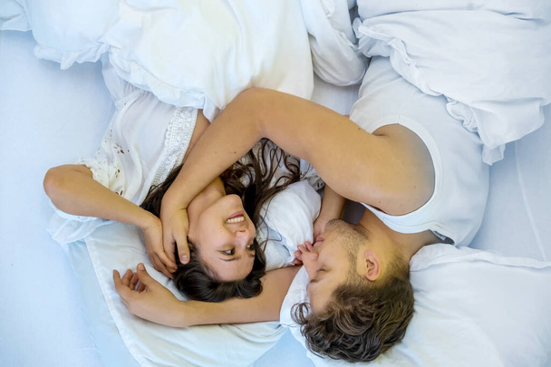 Upside down top view of an romantic, attractive, contented, young, hugging sexy loving couple in white bed, copy space - Photo, Image