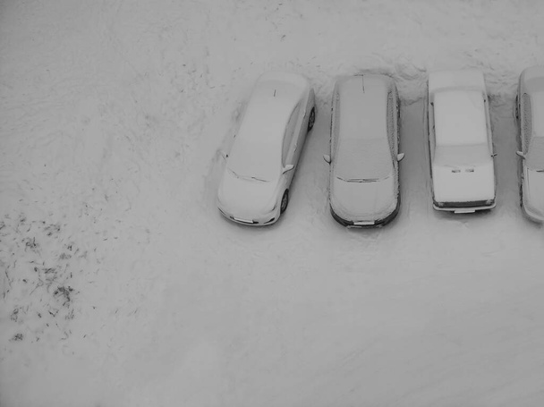 Ground parking cars after snowfall, view from above. Automobiles covered with snow. top view. Free space is on the winter parking lot in the line of snowy cars - Foto, afbeelding