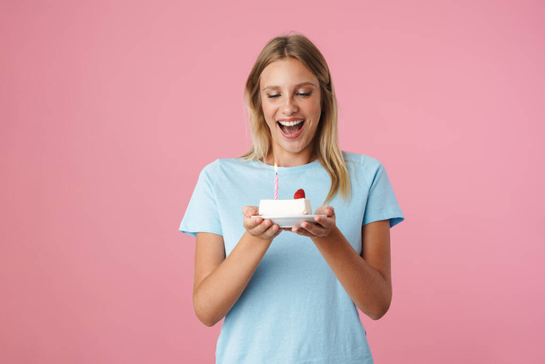 Happy beautiful girl smiling while posing with birthday cake isolated over pink background - Zdjęcie, obraz