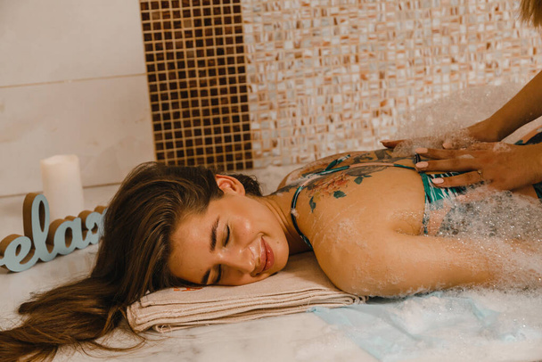 Lujoso masaje de espuma relajante en el hammam turco. Masajista arruga piel de mujer en hammam. - Foto, Imagen
