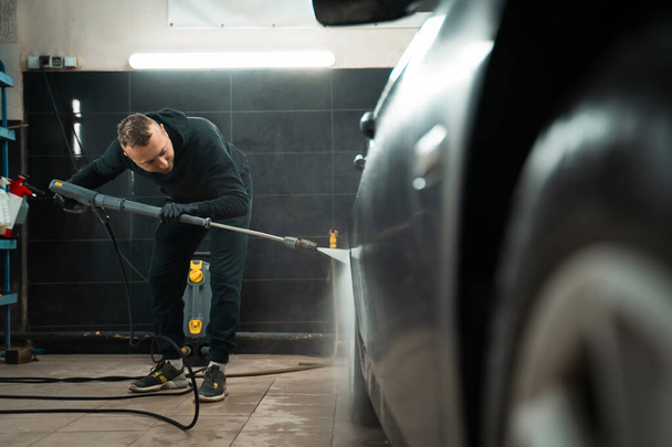 Professional car wash. Detailing employee washes car with pressure washer - 写真・画像
