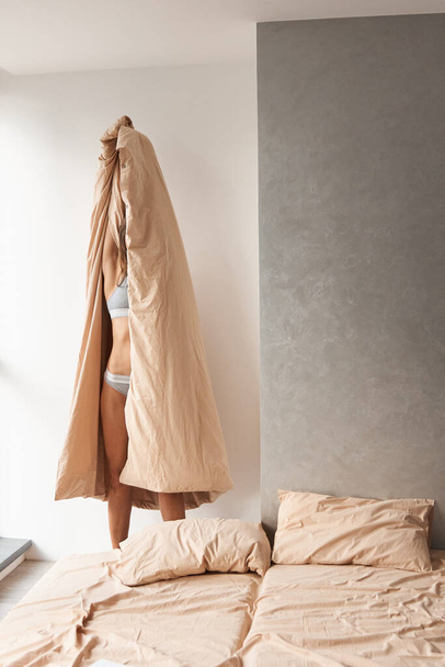 beautiful girl basks in natural beige cotton bedding near big bed - Zdjęcie, obraz
