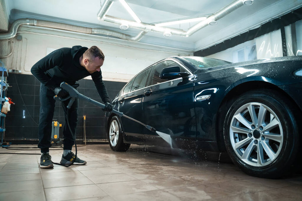 Professional car wash. Detailing employee washes car with pressure washer - Fotó, kép