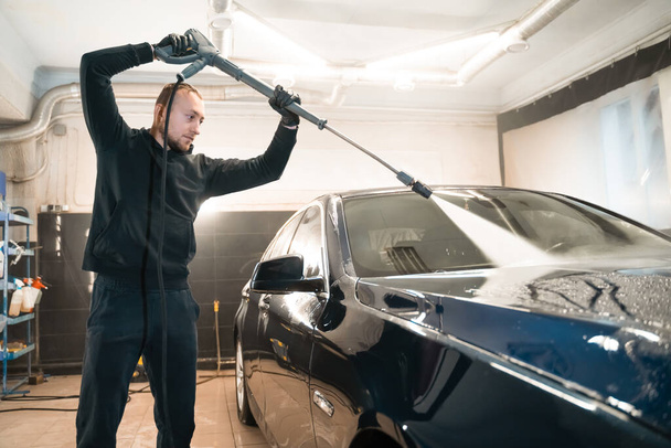 Professional car wash. Detailing employee washes car with pressure washer - Valokuva, kuva