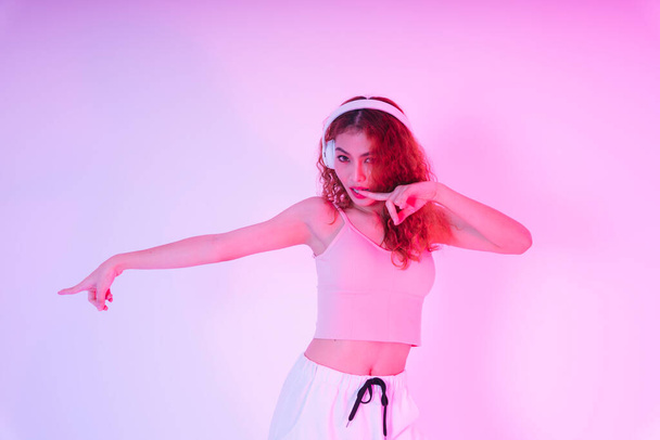 Νεαρή Ασιάτισσα που φοράει ακουστικά και χορεύει σε φόντο νέον φωτός. - Φωτογραφία, εικόνα
