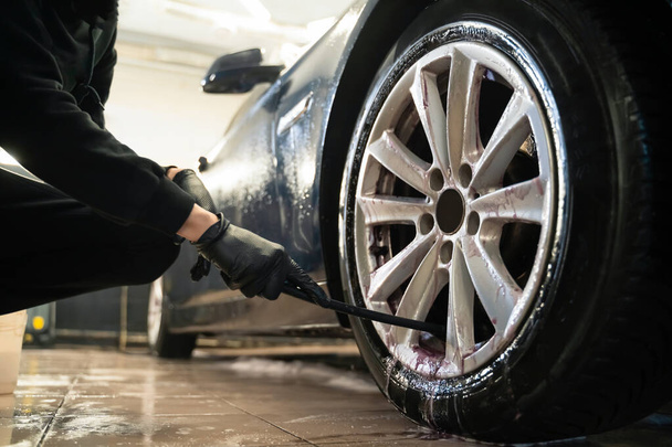 Λεπτομερής εργαζόμενος κέντρο καθαρίζει τροχούς αυτοκινήτων με βούρτσα. Διαδικασία καθαρισμού σώτρου τροχού οχήματος - Φωτογραφία, εικόνα