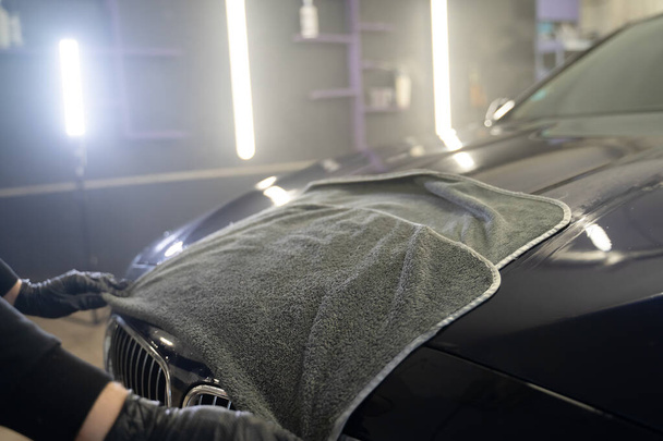 Auto wassen werknemer veegt de auto na het wassen met microvezel handdoek. Professionele carwash - Foto, afbeelding