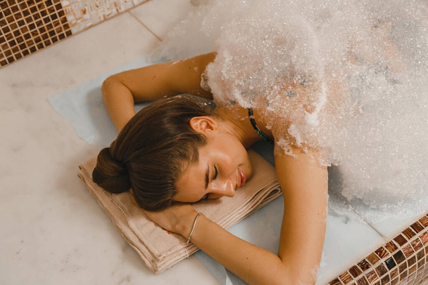 Lussuoso massaggio rilassante in schiuma nell'hammam turco. Massaggiatore sbriciola la pelle della donna in hammam. - Foto, immagini