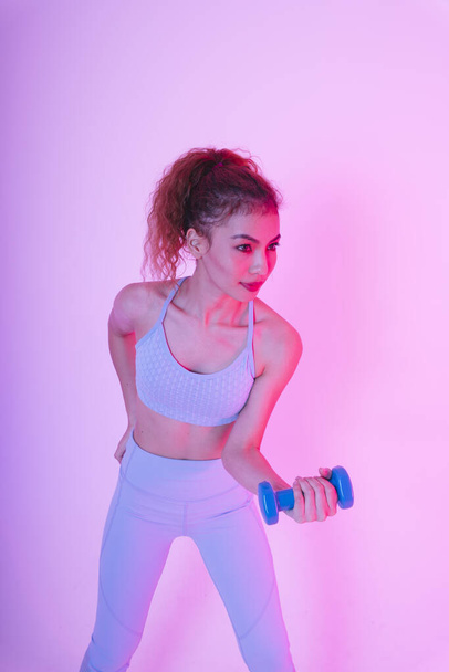 Saludable joven mujer asiática ejercicios con mancuerna sobre fondo de luz de neón. Concepto de gimnasio. - Foto, imagen