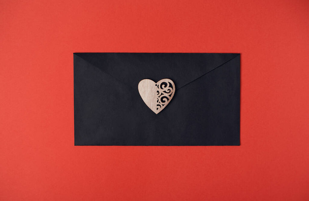 Kırmızı zemin üzerinde tahta kalp olan siyah bir zarf. Düz yerde, üst tarafta. Sevgililer Günü konsepti için romantik aşk mektubu. - Fotoğraf, Görsel