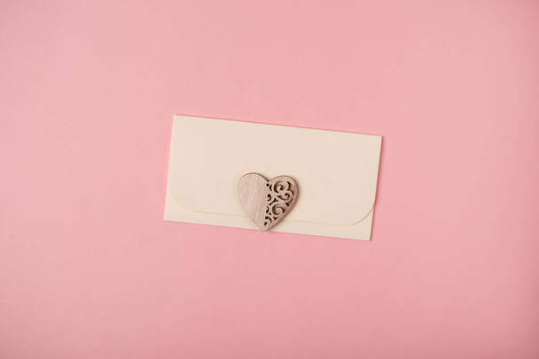 Envelope and wooden heart on the rose background. Flat lay. Romantic love letter for Valentine's day concept. - Foto, Imagen