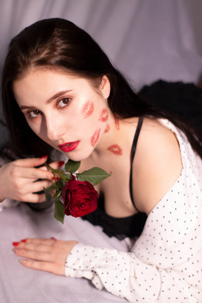 sexy brunette woman with kisses, lipstick marks on her face and neck, with red rose. girlfriend, date, relashionship. lesbian gay. lgbt. copy space - Zdjęcie, obraz
