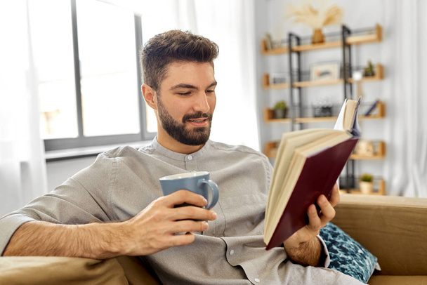 man reading book and drinking coffee at home - Photo, image