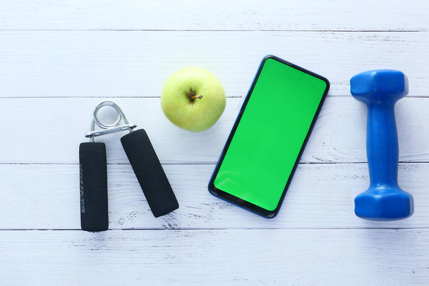  smartphone met sportuitrusting op witte houten achtergrond  - Foto, afbeelding