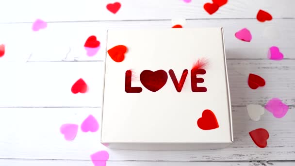 καρδιές πετούν στο κουτί δώρου με τη λέξη Αγάπη. παρουσία σε λευκό φόντο ξύλο για την ημέρα του Αγίου Βαλεντίνου. - Πλάνα, βίντεο