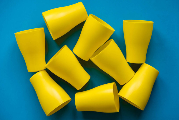 Muchas tazas de plástico amarillo sobre fondo azul. Listos para la fiesta. Vista superior. Estilo minimalista. Copiar, espacio vacío para texto. - Foto, Imagen