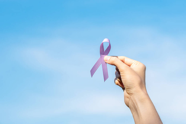 世界がんデー(2月4日) 。女性の手は、生活や病気をサポートするためのラベンダー紫色のリボンを保持。医療・医療の概念 - 写真・画像